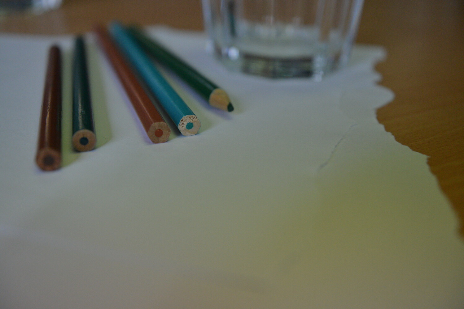 Some coloured pencils and a glass on a sheet of ripped paper